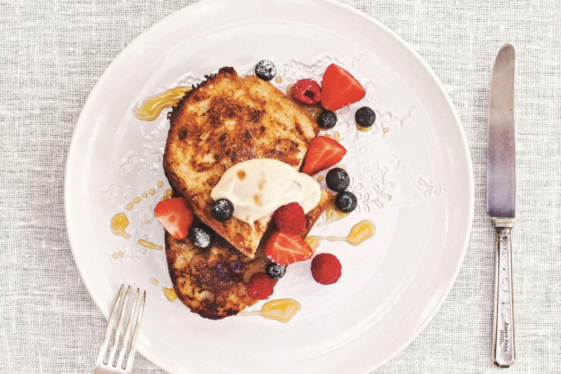 Plate of vegan French toast with non-dairy cream, berries, and maple syrup on a white plate. 