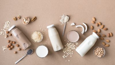 Various vegan plant based milk and ingredients on beige, top view, copy space. Dairy free milk substitute drink, healthy eating.