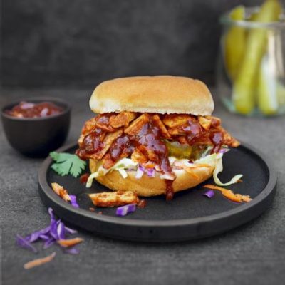 Sweet Earth's Pulled Chipotle Chikn Slider bursting out of a vegan bun on a black plate